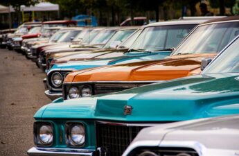 Classic American cars in turquoise, orange, and white lined up at a vintage car gathering.