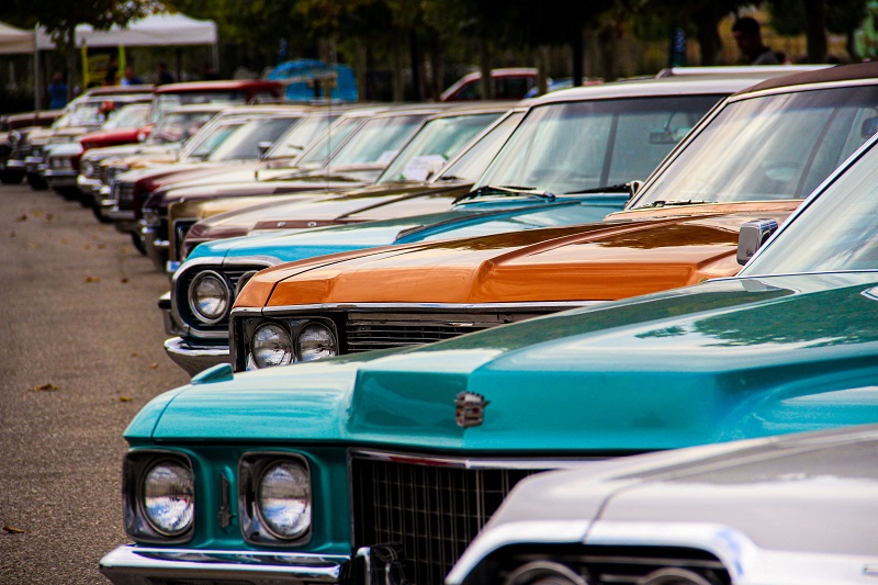Classic American cars in turquoise, orange, and white lined up at a vintage car gathering.